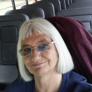 A stage 2 breast cancer survivor named Deb smiles while sitting on the school bus she drives as part of her job. 