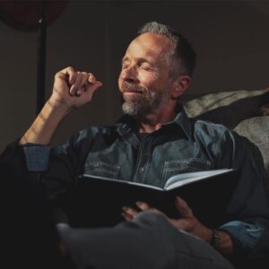 Dr. Jeff Myers holds an open book and closes his eyes contemplatively in a chair. 