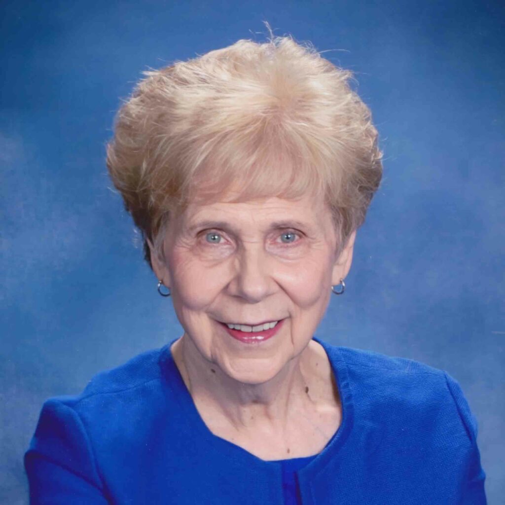 Sue McGee, cancer survivor, smiles for a photo with a blue background.